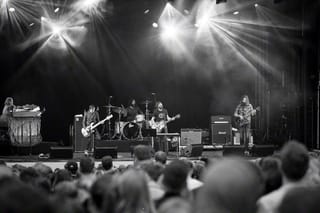 Black-and-white photo of Band of Horses on an outdoor stage under bright lights, seen from behind the crowd