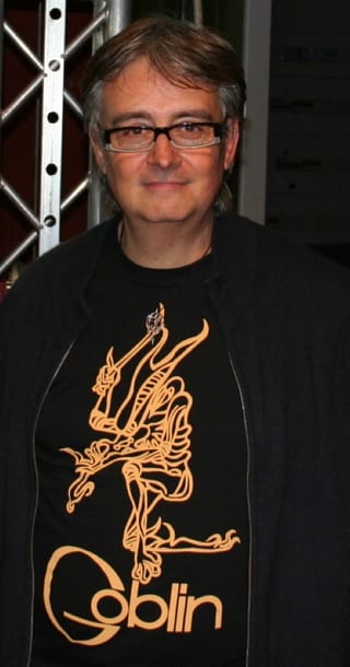 Claudio Simonetti in glasses and a black Goblin T-shirt, standing backstage