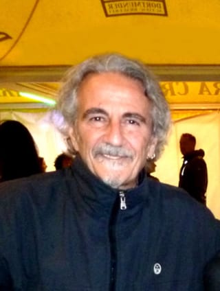 Fabio Pignatelli, grey-haired and smiling, in a dark zip-up jacket under a festival tent