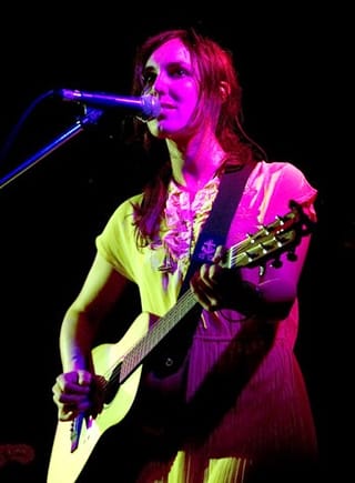 Holly Throsby in a yellow dress singing into a microphone with an acoustic guitar