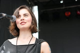 Leanne Macomber at a microphone on an outdoor stage, in a black sleeveless top
