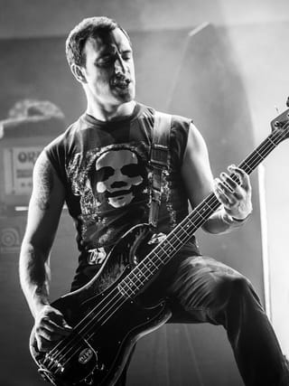 Black-and-white photo of Stephen Brodsky in a sleeveless T-shirt playing a bass guitar on stage