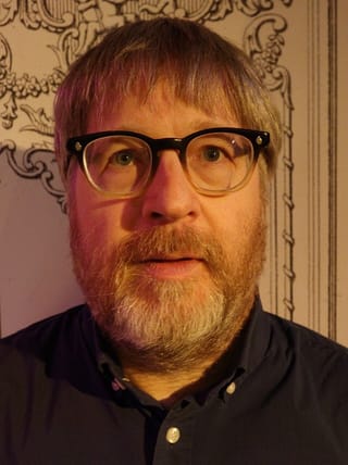 Close-up of Steve Shelley, grey-bearded and wearing glasses and a dark shirt
