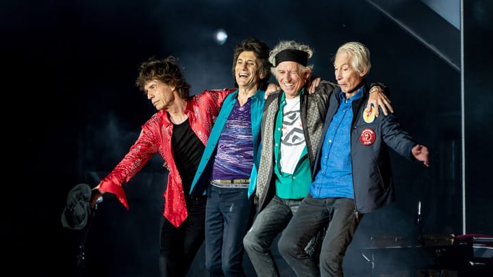 Mick Jagger, Ronnie Wood, Keith Richards and Charlie Watts bowing arm in arm on a dark stage