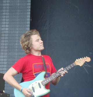 Ty Segall in a red T-shirt playing a light-blue electric guitar on an outdoor stage