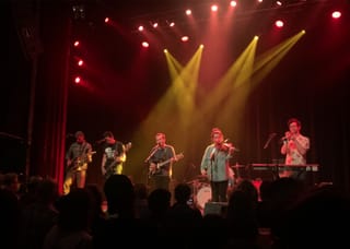 Typhoon on stage under red and yellow spotlights, with three guitarists, a violinist and a trumpet player at the front