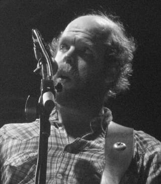 Black-and-white close-up of Will Oldham singing into a microphone, in a checked shirt
