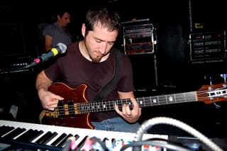 Zach Smith playing a wooden bass guitar behind a keyboard on a dark stage
